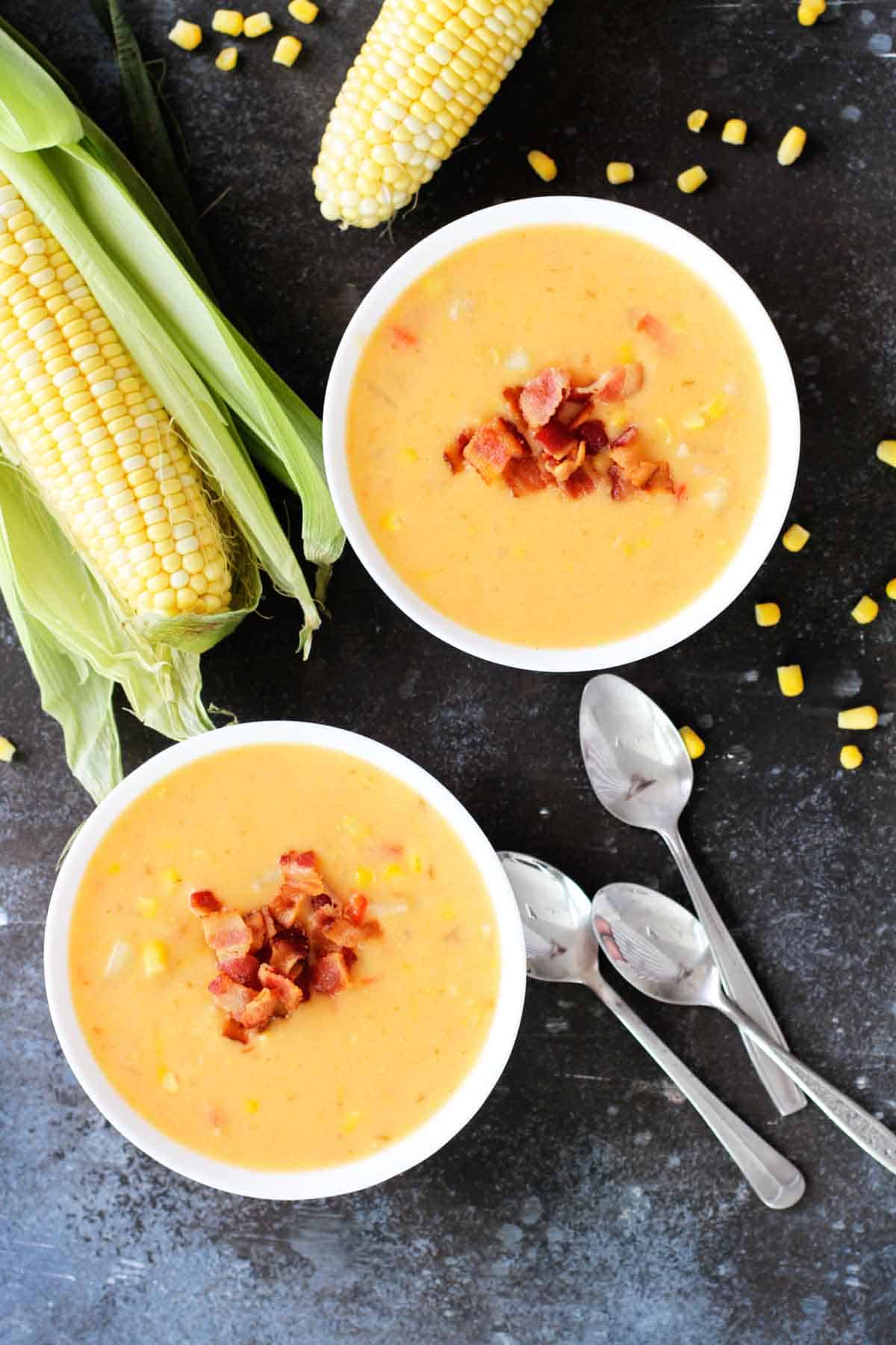 Bowls of corn chowder with bacon with fresh corn on the side.