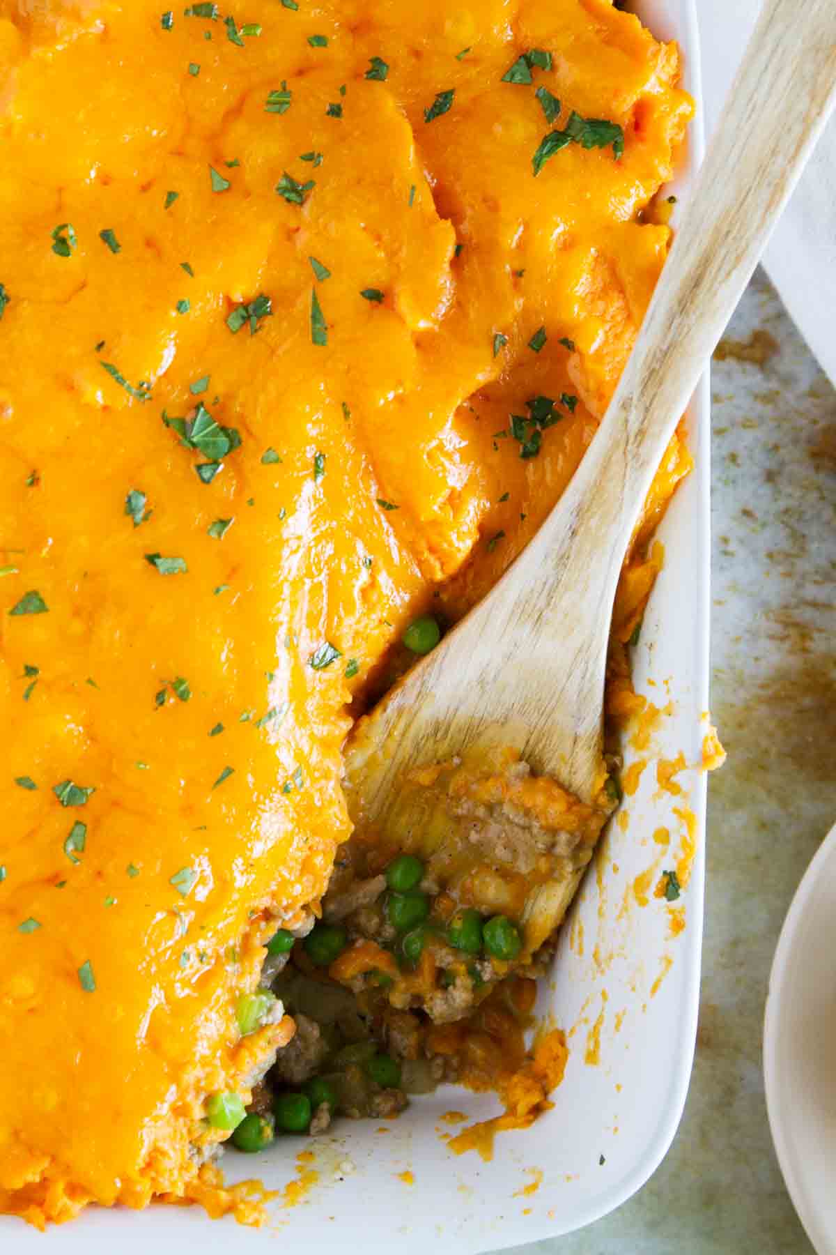 Baking dish with Turkey Shepherd's Pie with Sweet Potatoes with a wooden spoon scooping some out.