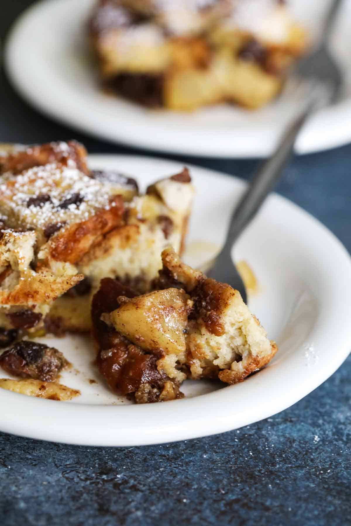 Slice of baked French toast casserole with apples and raisins with a bite taken from it.