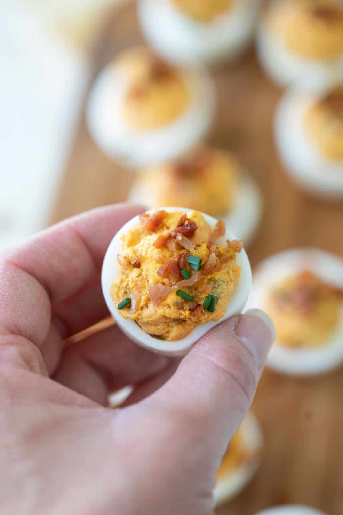 Hand holding a deviled egg with bacon.