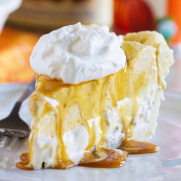 Slice of pumpkin and butter pecan ice cream pie on a plate with whipped cream.