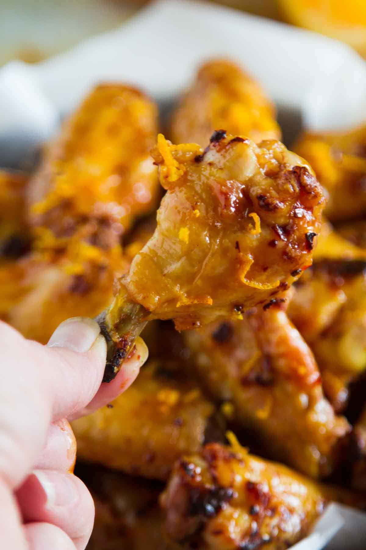 Holding up a single chipotle orange chicken wing with more in the background.