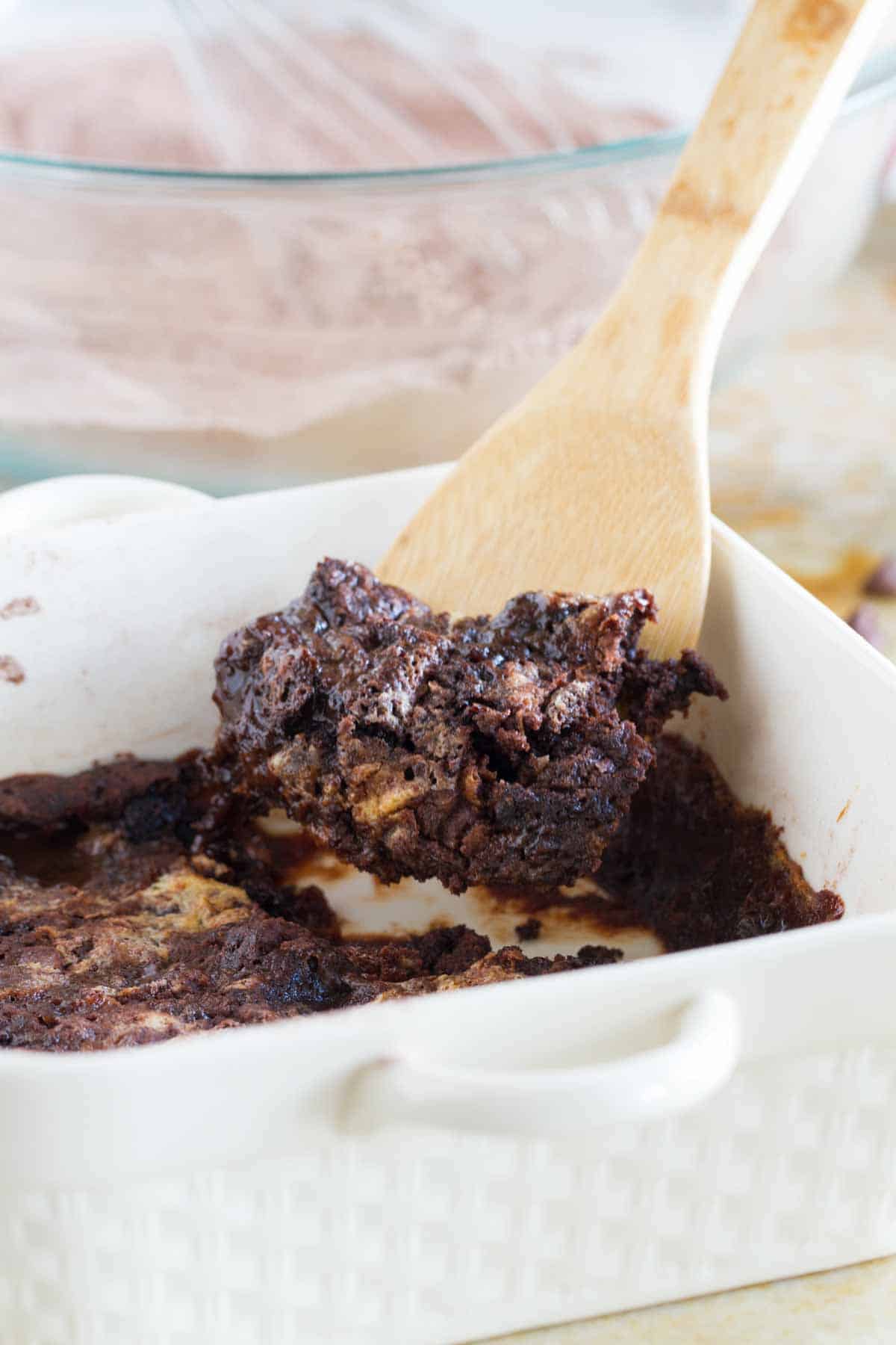 Scooping out chocolate dump cake from a baking dish.