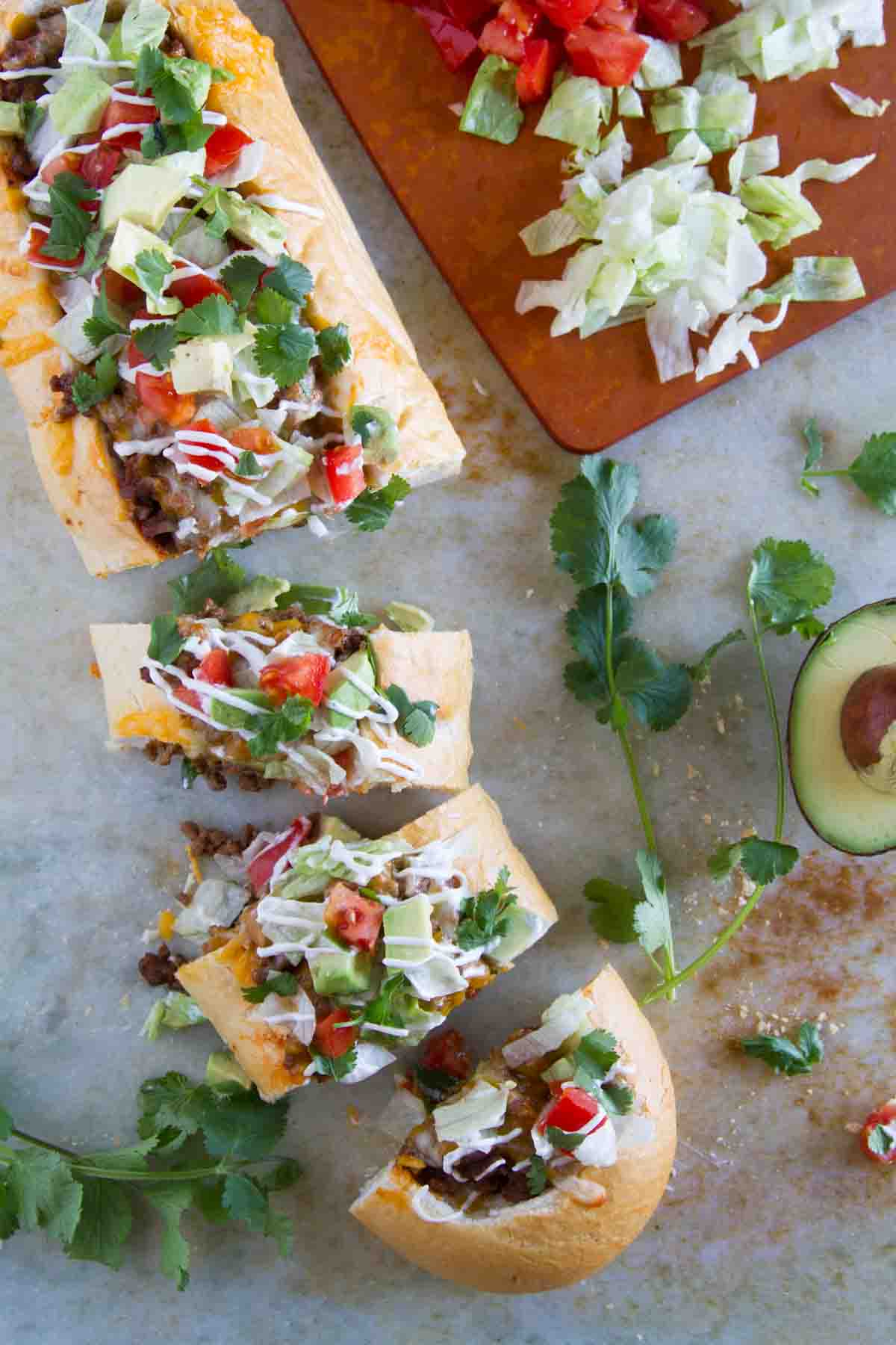 Loaf of Taco French Bread Pizza cut into pieces, topped with lettuce, tomatoes, cilantro, and sour cream.