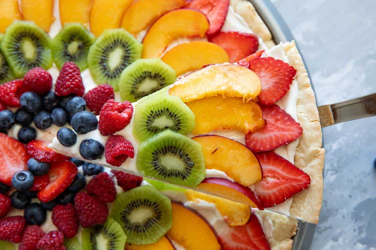 Slice of fruit pizza topped with strawberries, peaches, kiwi, and berries.
