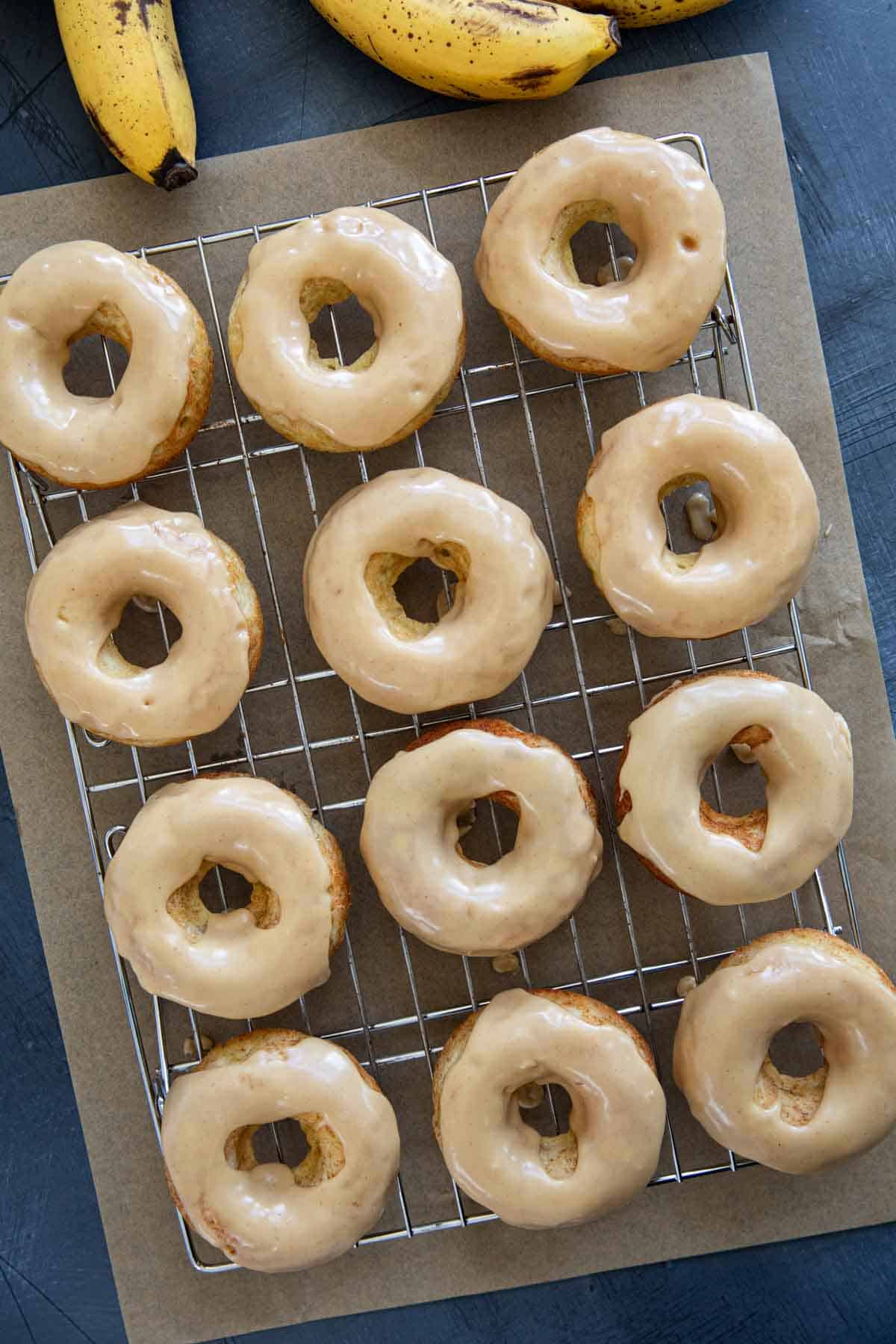 Banana donuts frosted with peanut butter icing on a cooling rack.
