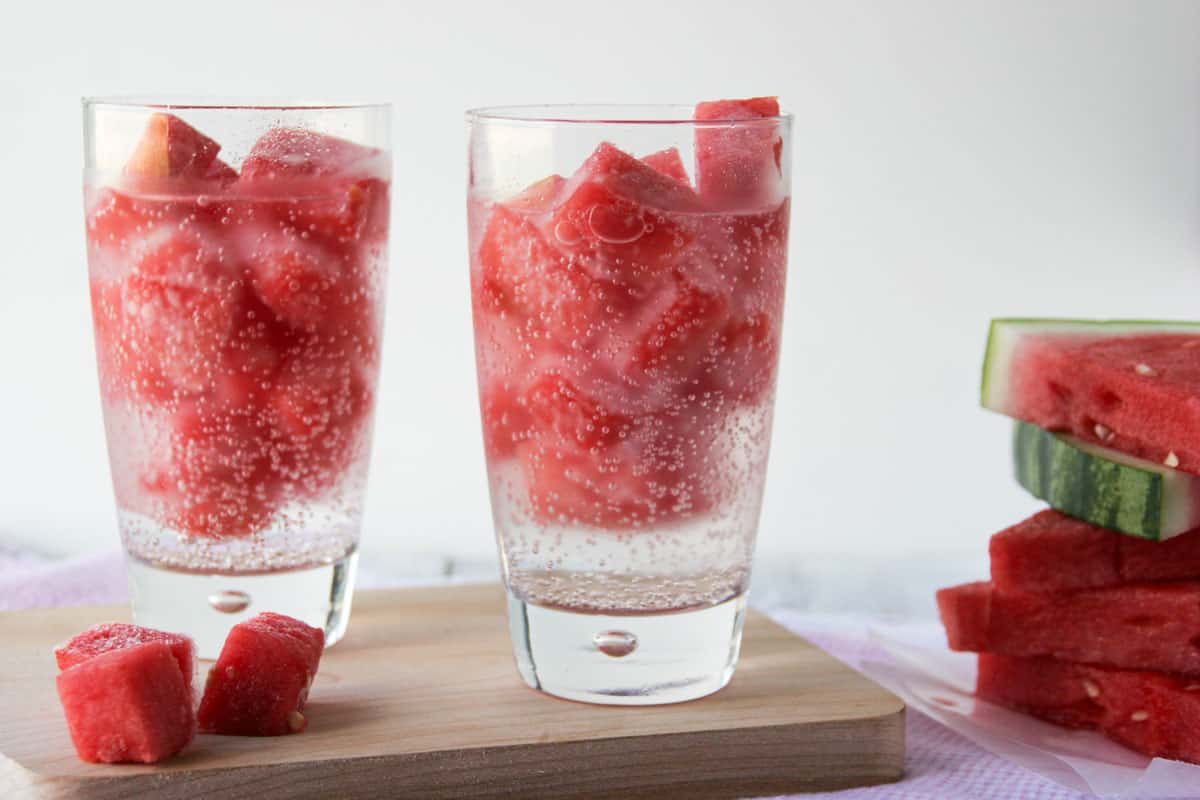Two glasses filled with watermelon ice and clear bubbly beverage.
