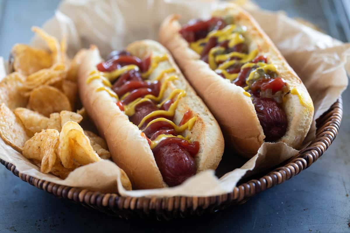 Air Fryer Hot Dogs topped with ketchup and mustard served with potato chips.