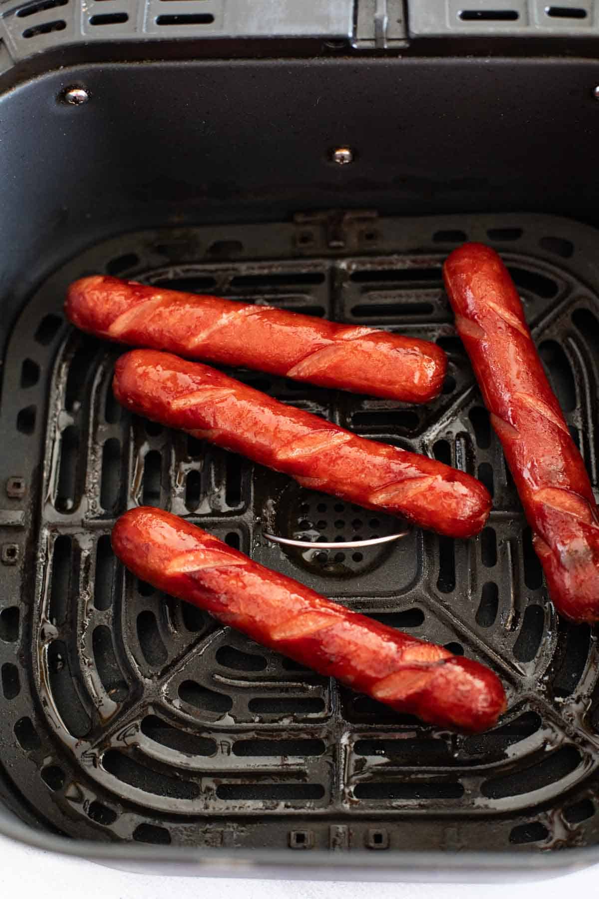 Cooked hot dogs in an air fryer basket.