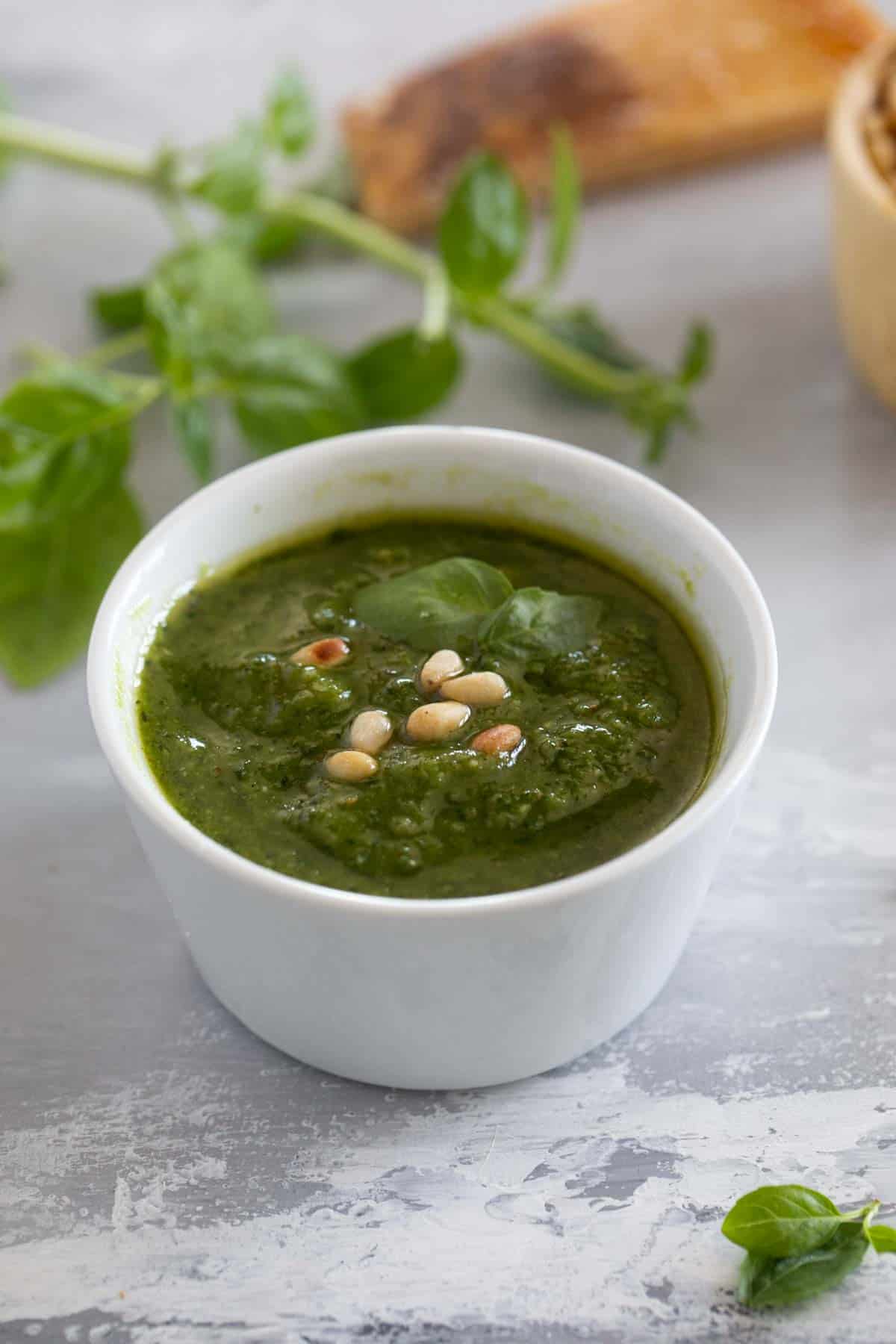 Small bowl filled with basil pesto, topped with pine nuts and fresh basil.