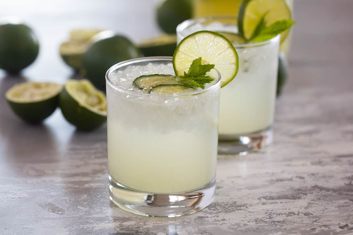 Two glasses of cucumber limeade with fresh limes.