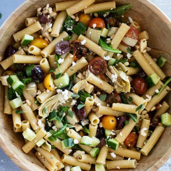 Wooden bowl full of Mediterranean Pasta Salad with pasta, olives, feta, and more.