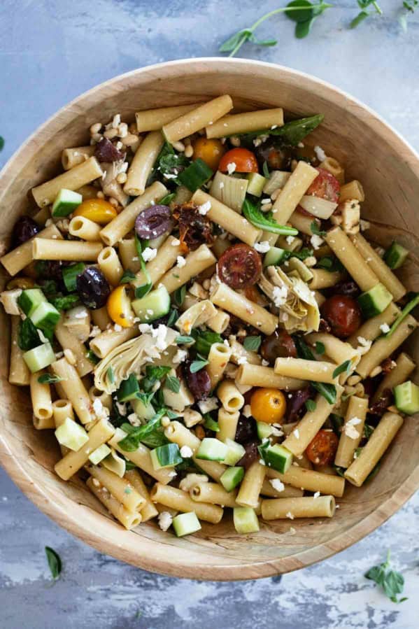 Wooden bowl full of Mediterranean Pasta Salad with pasta, olives, feta, and more.