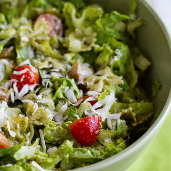 Bowl filled with pesto pasta and ham salad with romaine and tomatoes.