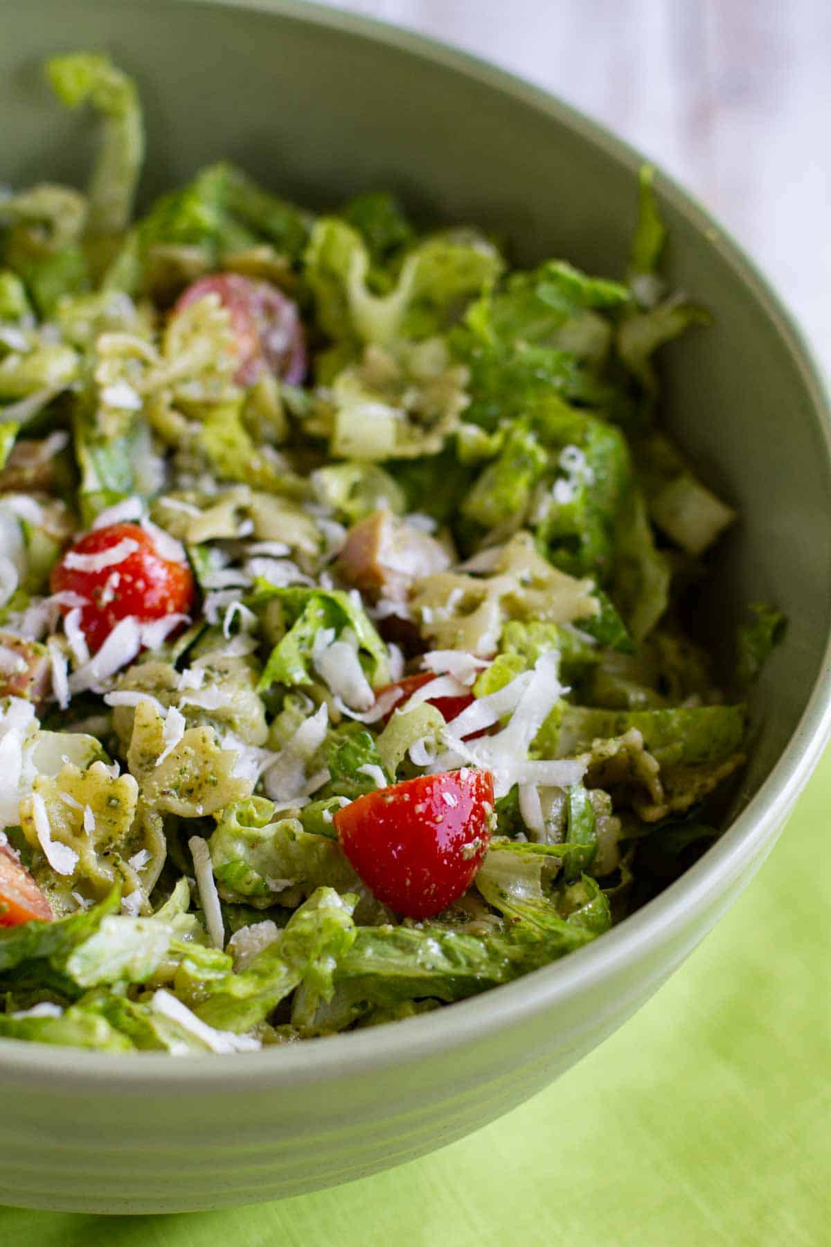 Bowl filled with pesto pasta and ham salad with romaine and tomatoes.