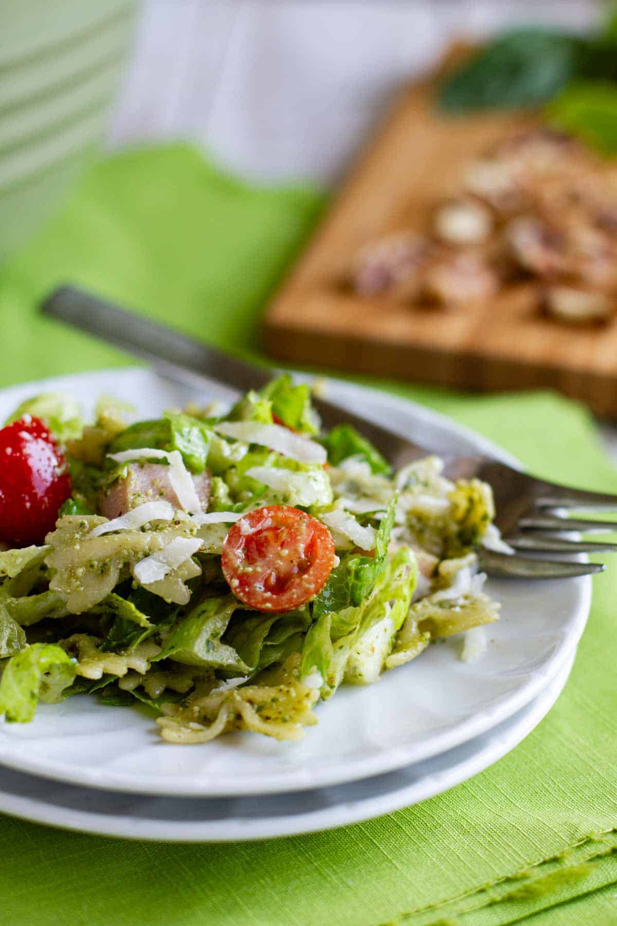 Serving of pesto pasta and ham salad on a plate with a fork.