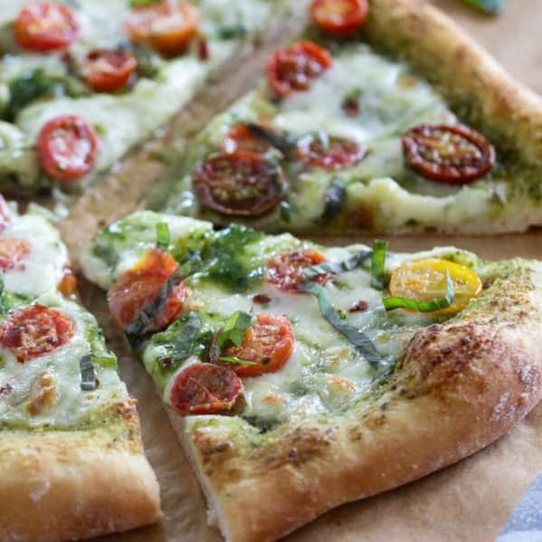 Pesto Pizza with tomatoes and fresh basil cut into slices.