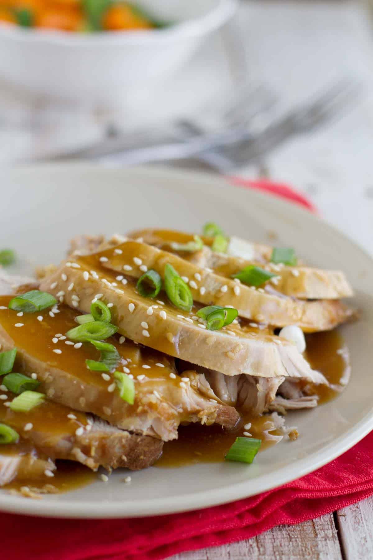 Plate with slices of sesame pork roast that are topped with a simple sauce and sesame seeds.