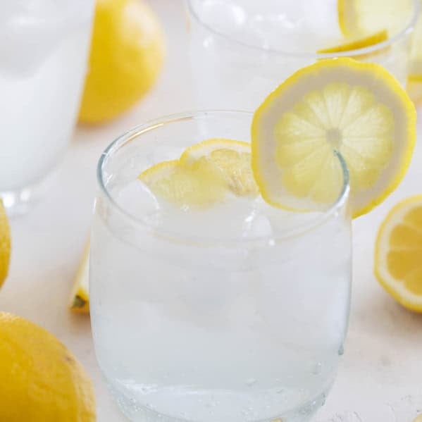 Glass of sweet lemon water with fresh lemons on top.