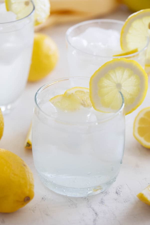 Glass of sweet lemon water with fresh lemons on top.