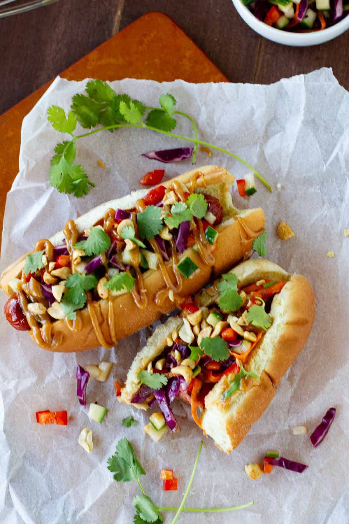 Two Thai Style Hot Dogs with a bite taken from one.