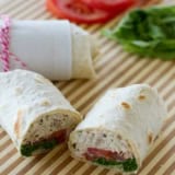 Chicken pesto wrap with tomato and lettuce, cut in half.