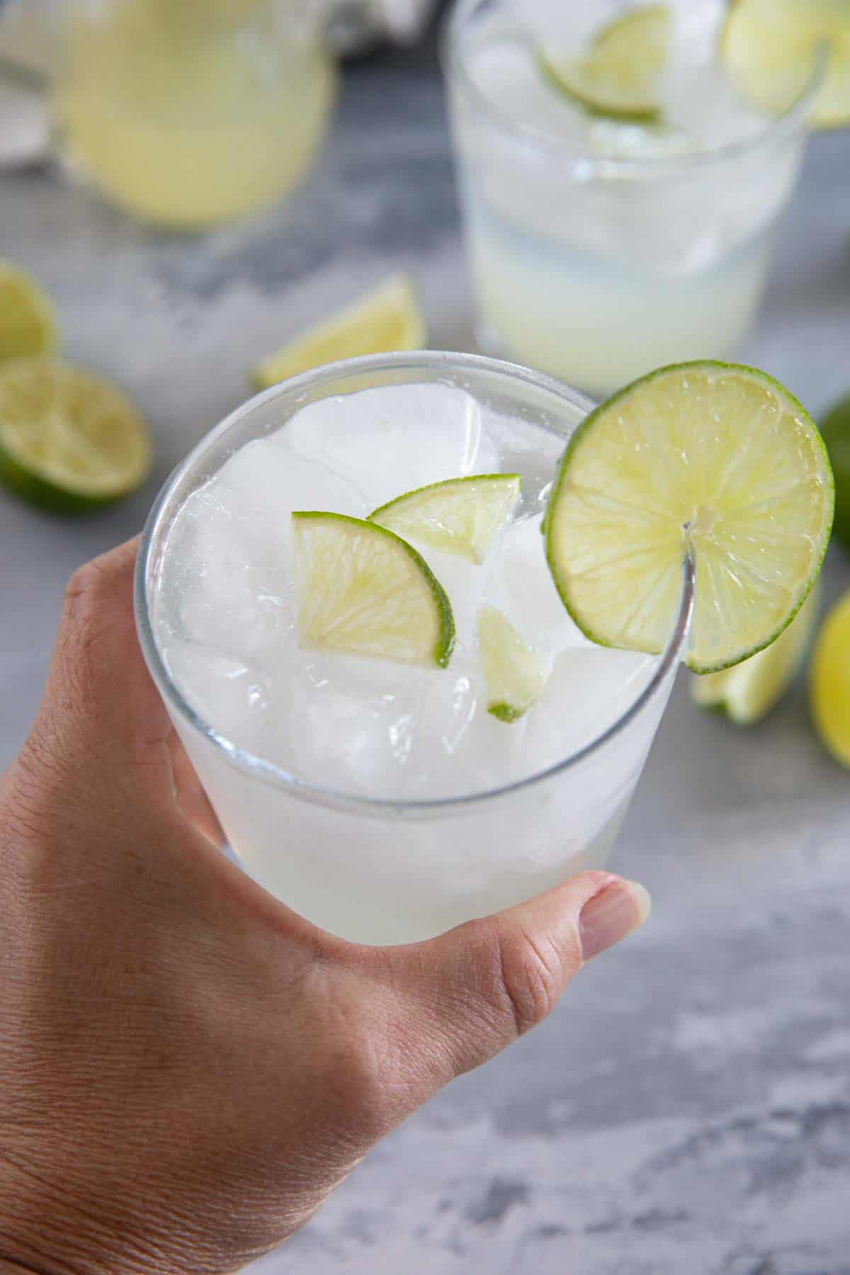 Hand holding a glass of ginger limeade with lime slices.