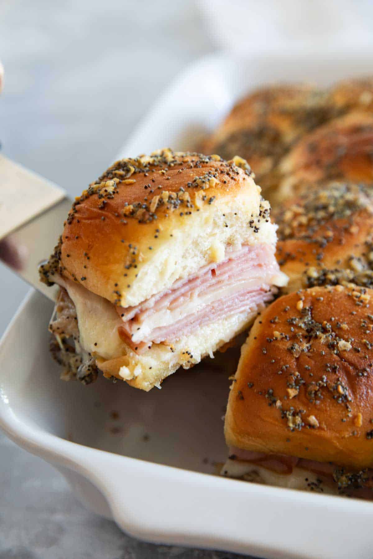 Taking a ham and cheese slider from a casserole dish.