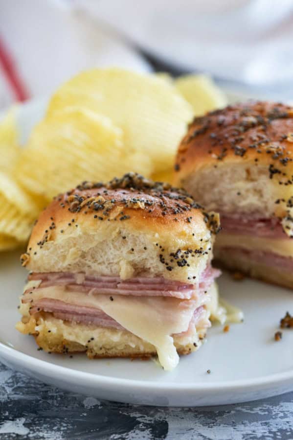 Two ham and cheese sliders on a plate with potato chips.