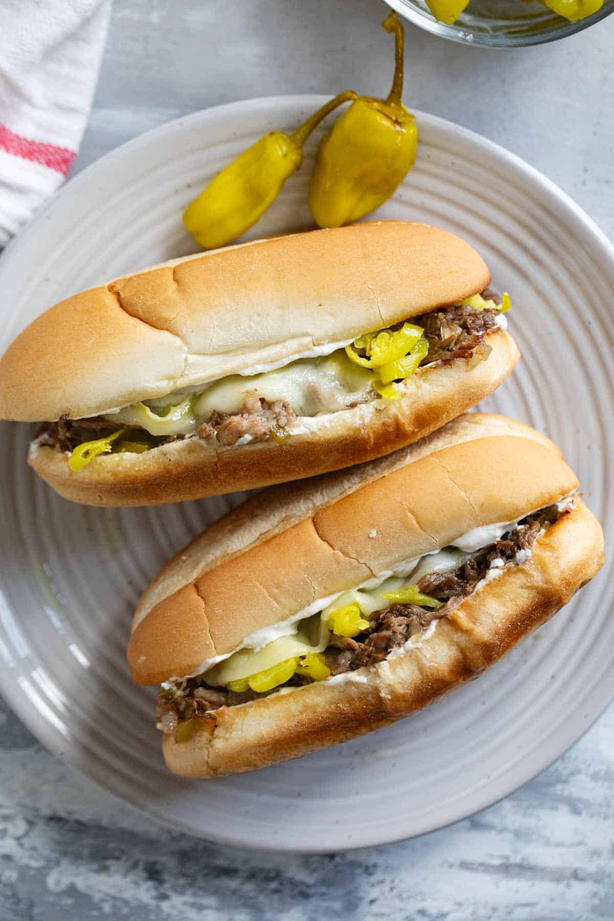 Two Italian Beef Sandwiches on a plate with pepperoncini peppers.