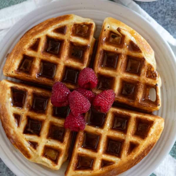 Belgian Waffle Recipe topped with syrup and fresh raspberries.