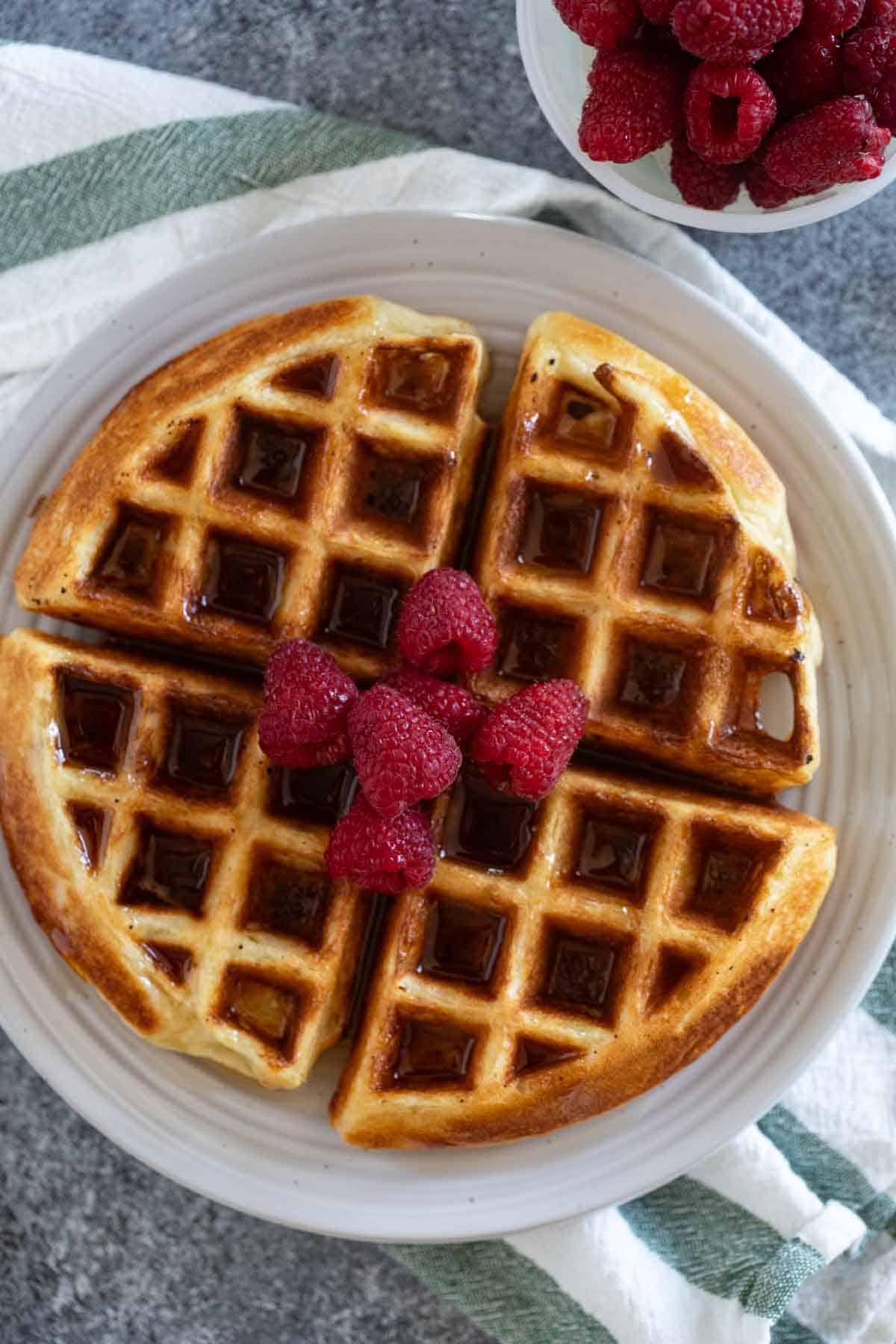 Belgian Waffle Recipe topped with syrup and fresh raspberries.