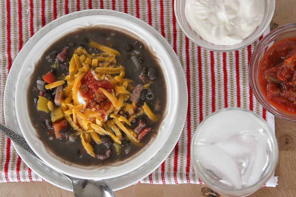 Bowl of black bean and ham soup topped with cheese, sour cream, and salsa.