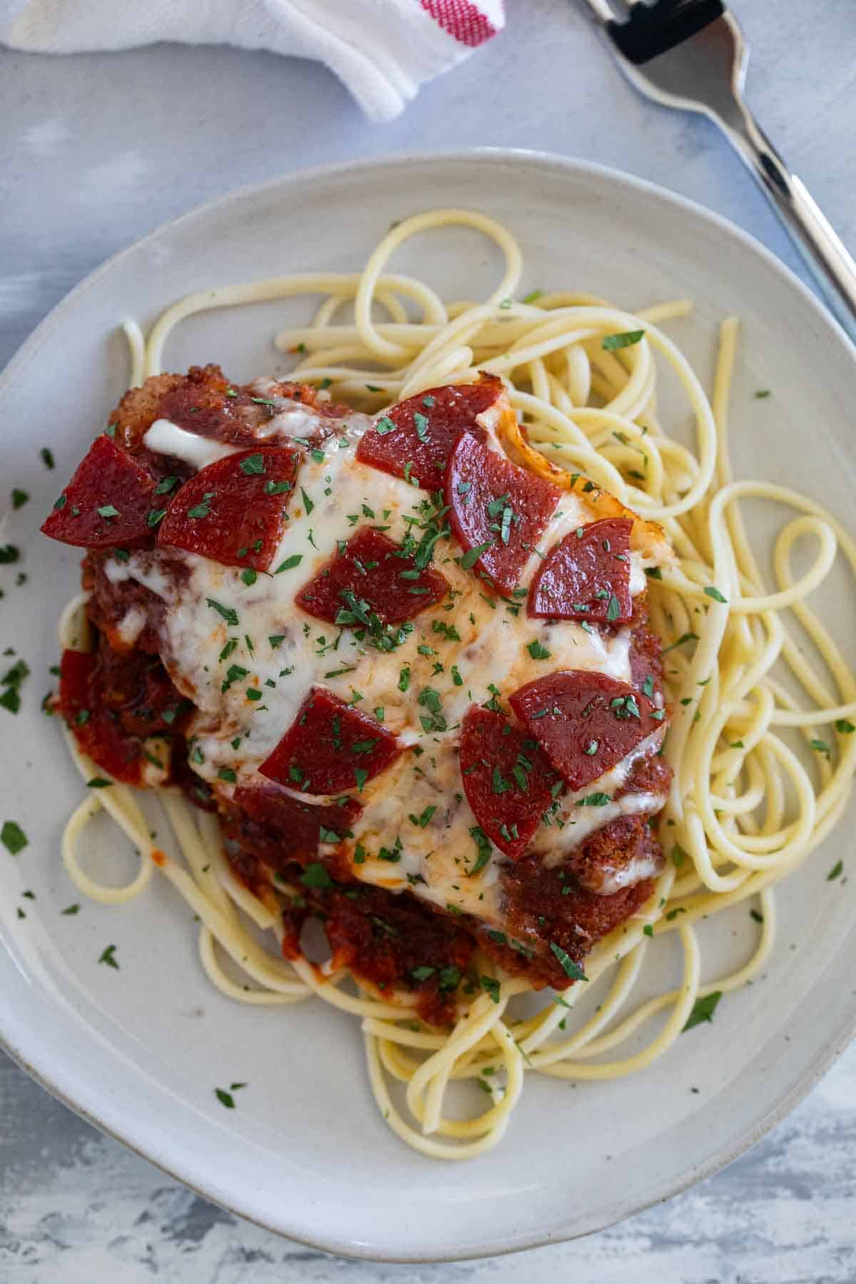 Chicken pepperoni served over spaghetti on a white plate.