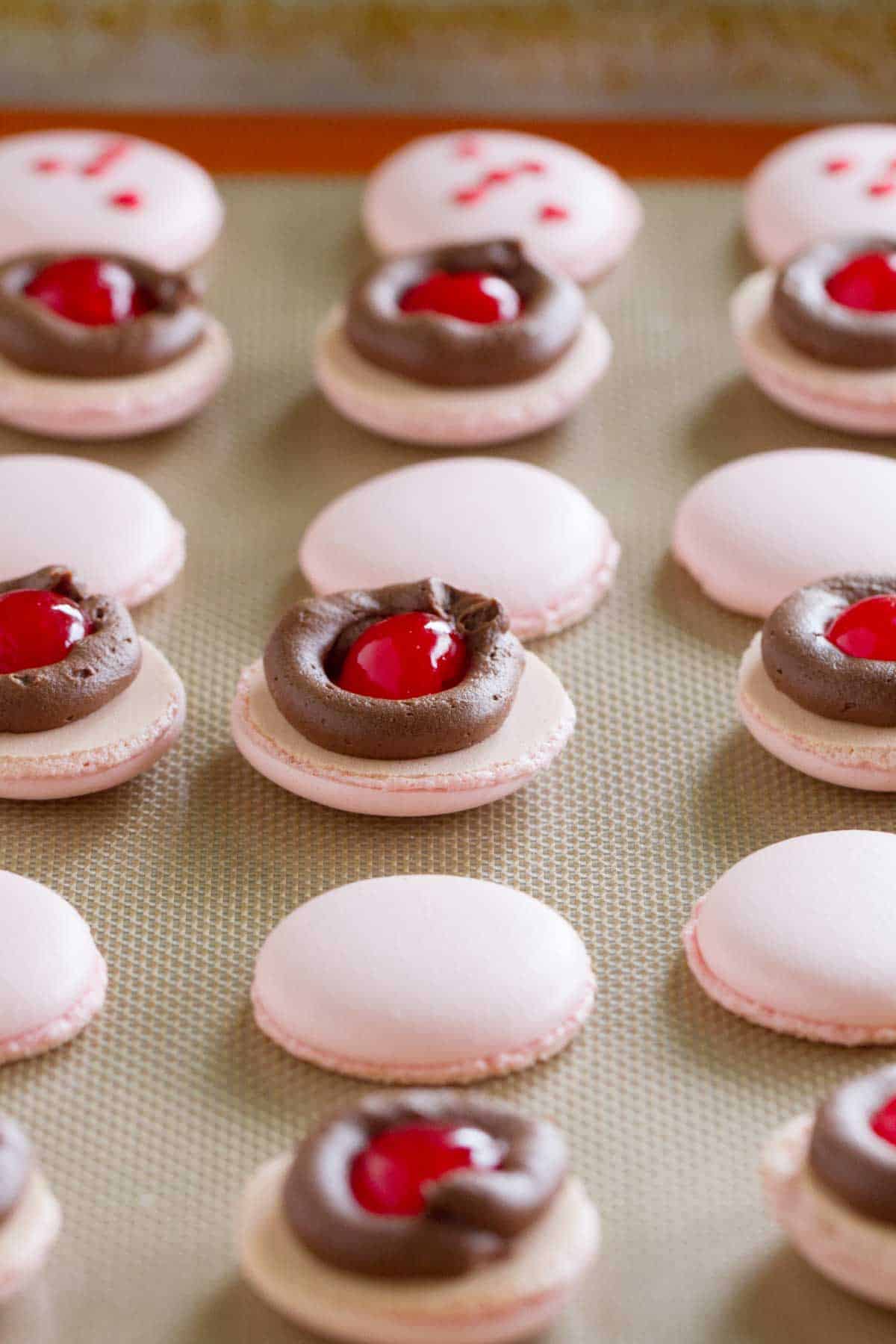 Macarons filled with chocolate and a maraschino cherry.