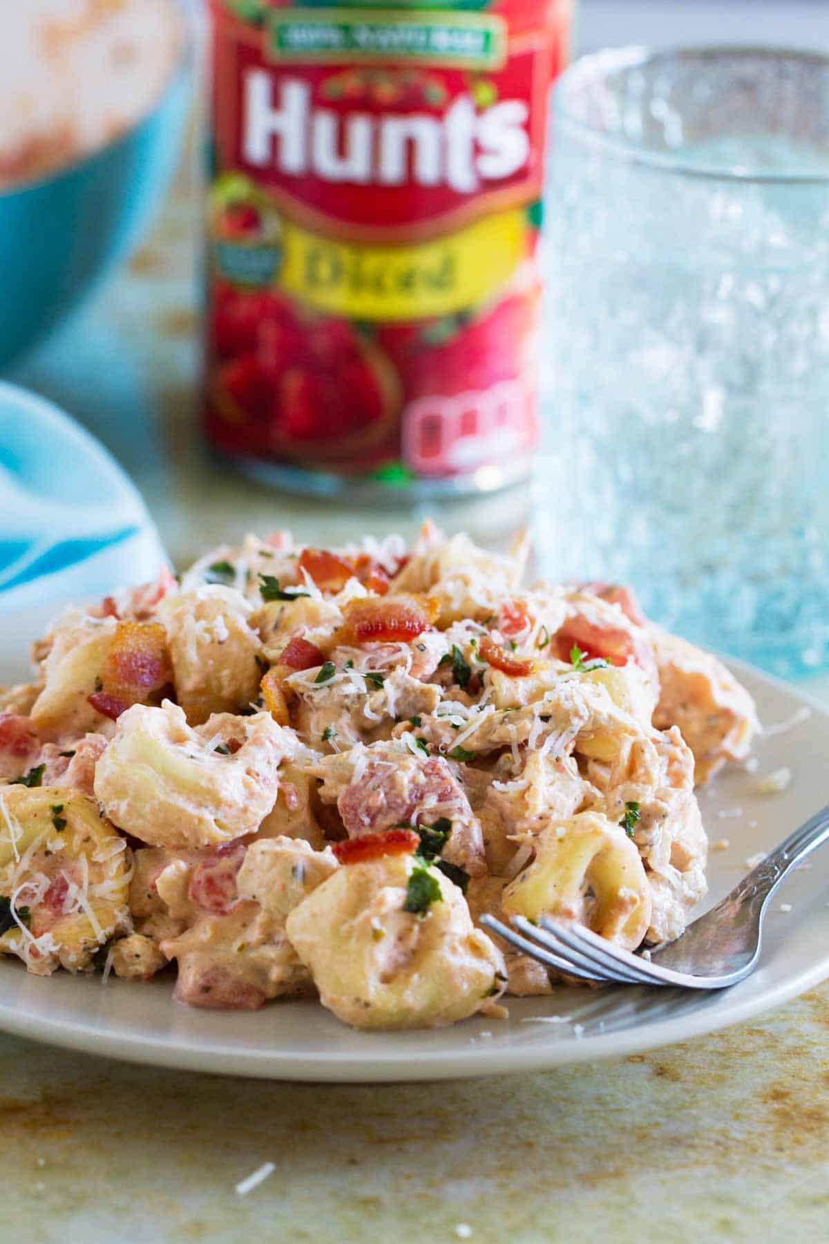 Plate filled with Creamy Tomato Tortellini with Chicken and Bacon with a can of tomatoes in the background.