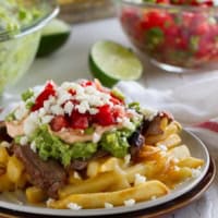 Plate filled with Enchilada Steak Fries - French fries topped with cheese, guacamole, pico de Gallo, and enchilada marinated steak.