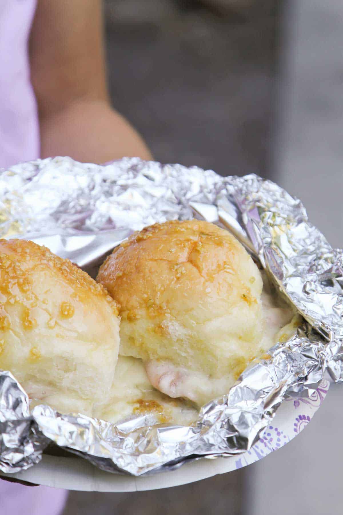 Two Hot Ham and Cheese Campfire Sandwiches in foil on a paper plate.