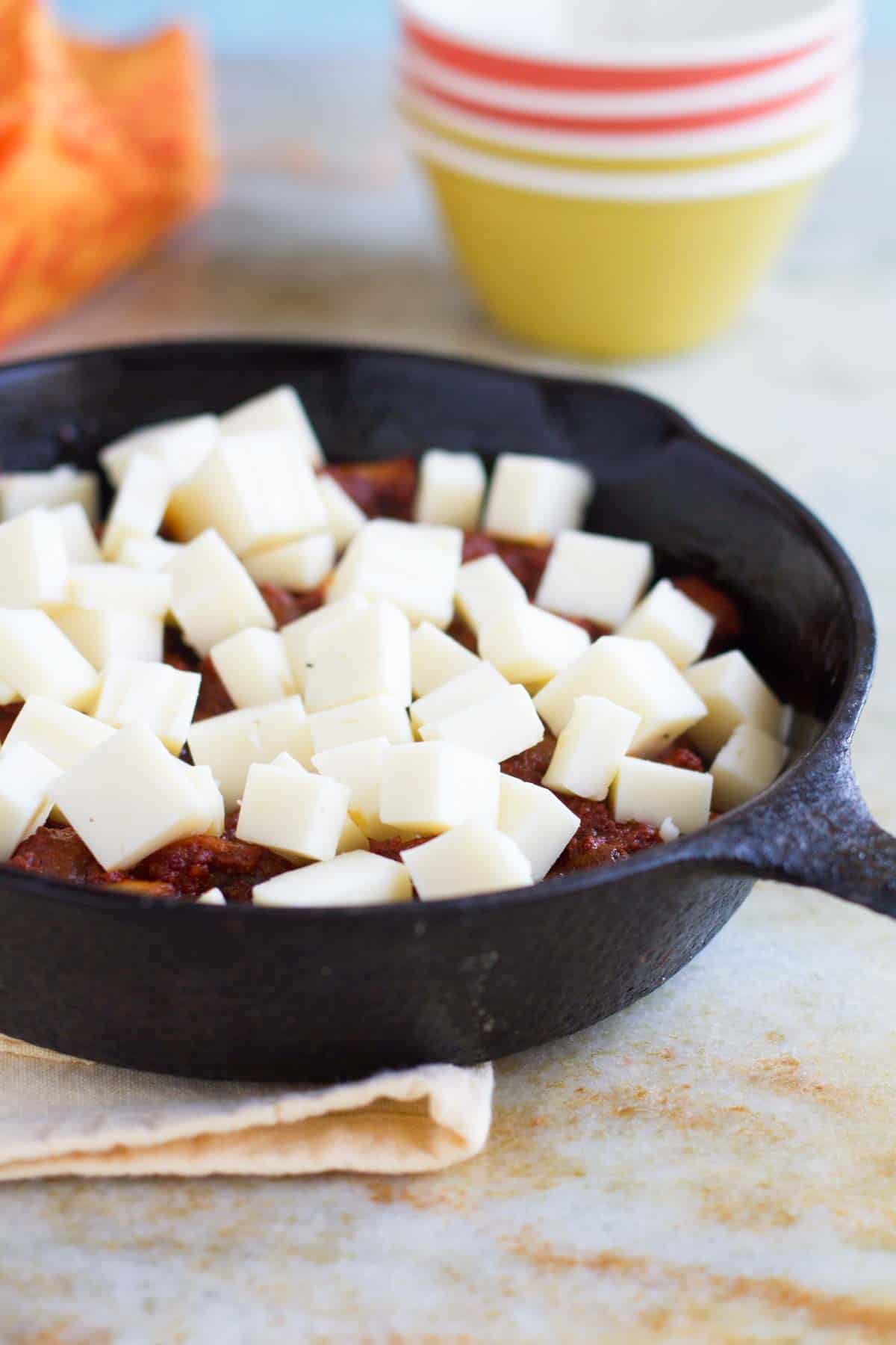 Cubes of cheese on top of chorizo and mushrooms.