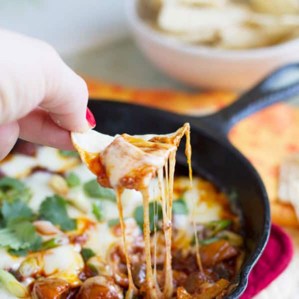 Hand with a tortilla chip dipping into Mushroom and Chorizo Queso Dip.