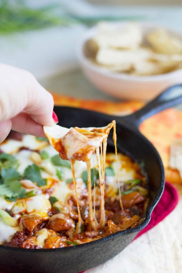 Hand with a tortilla chip dipping into Mushroom and Chorizo Queso Dip.