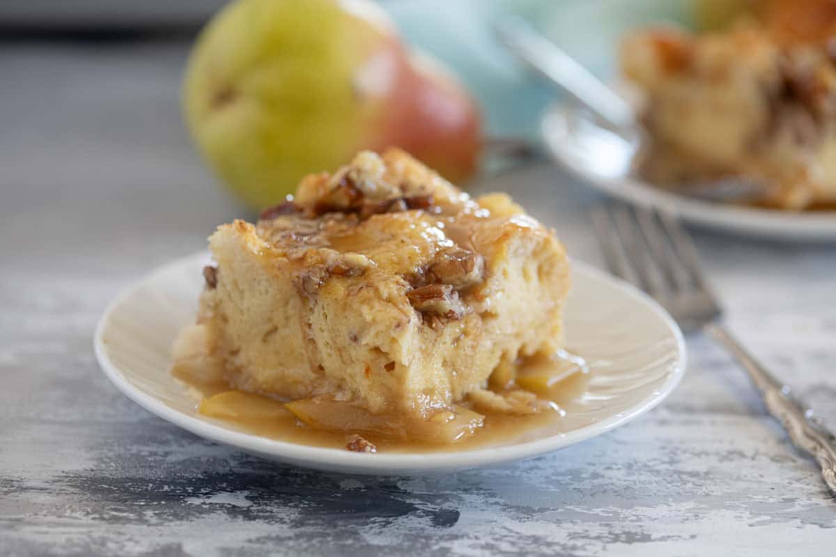 Slice of Pear Baked French Toast on a plate with a pear in the background.