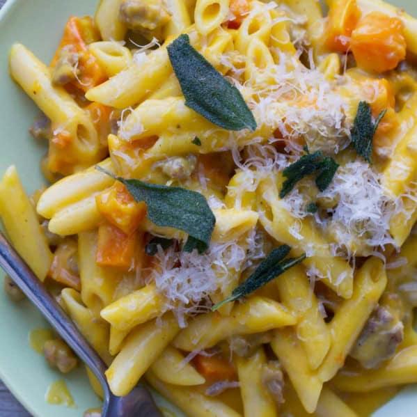 Plate filled with Penne with Butternut Squash and Sausage and topped with parmesan cheese and sage.