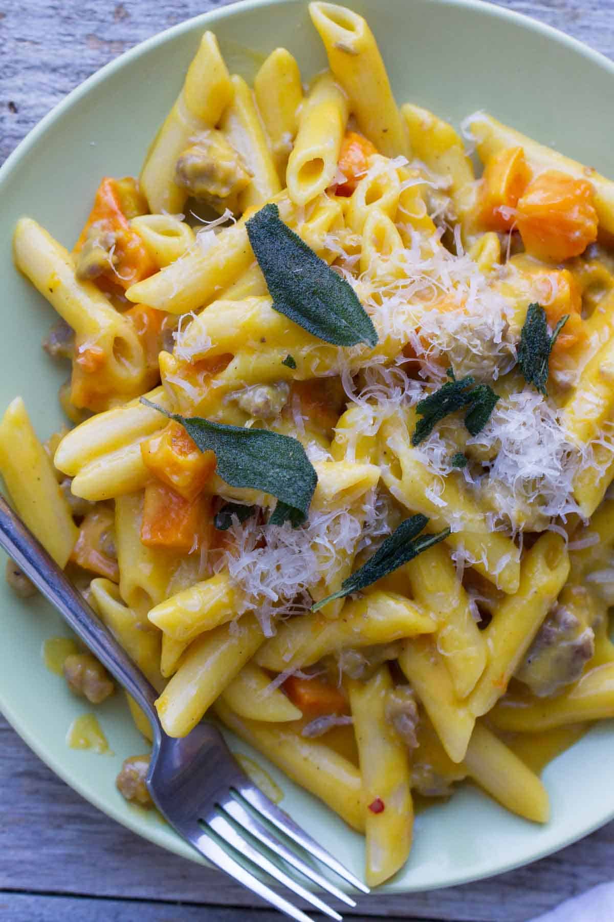 Plate filled with Penne with Butternut Squash and Sausage and topped with parmesan cheese and sage.