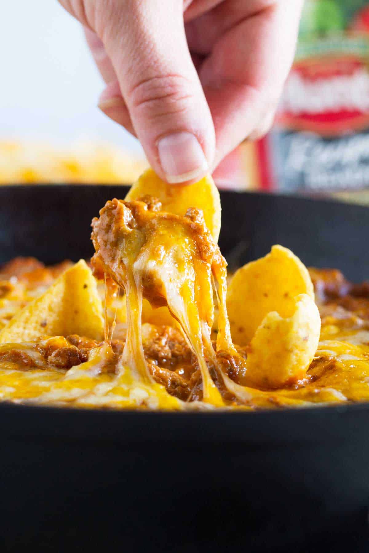 Person holding a chip and dipping into Sloppy Joe Dip, showing cheese pull.