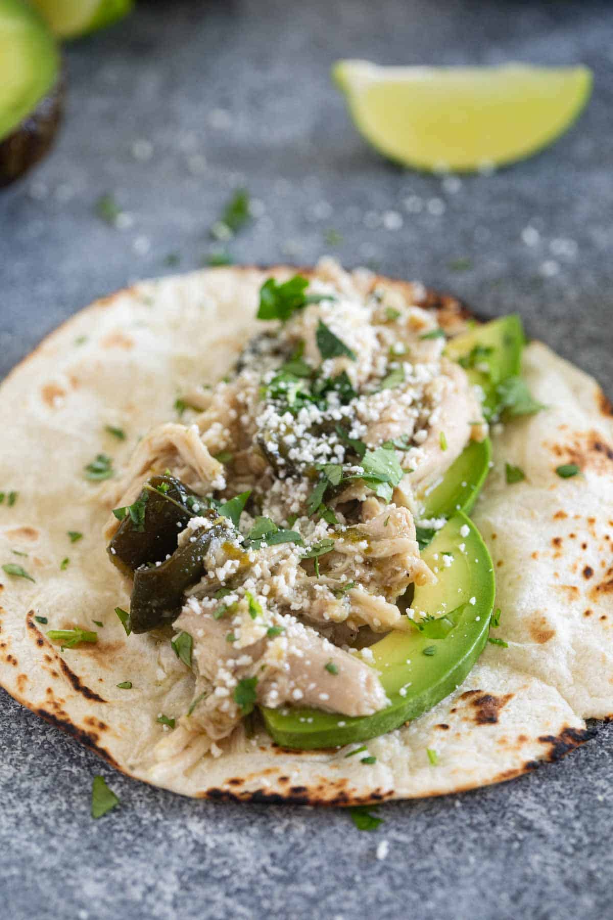 Open taco with avocado, slow cooker chicken, cotija cheese, and cilantro.