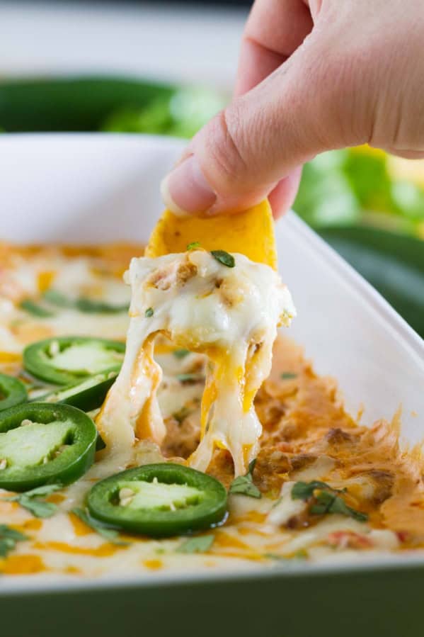 Using a chip to get a cheesy bite of spicy sausage dip, showing cheese pull.