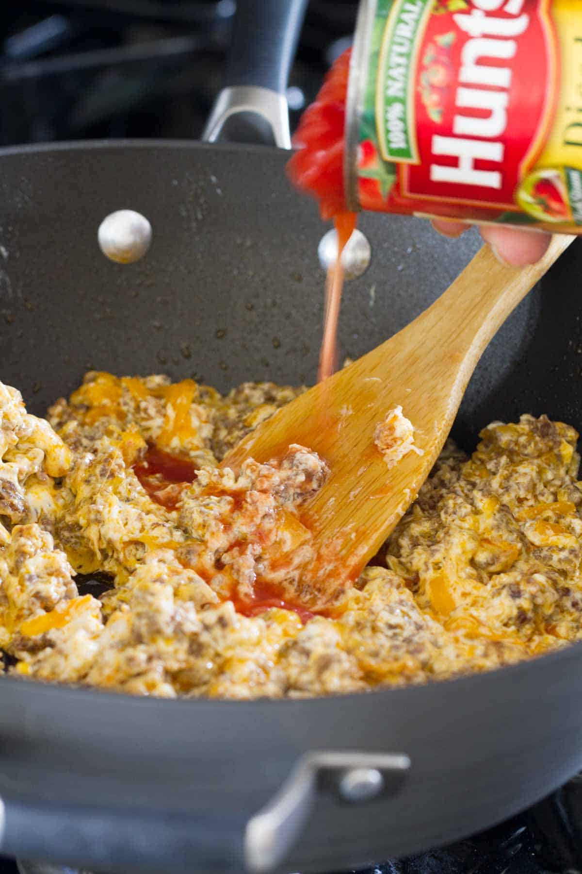 Adding canned tomatoes into spicy sausage dip mixture.