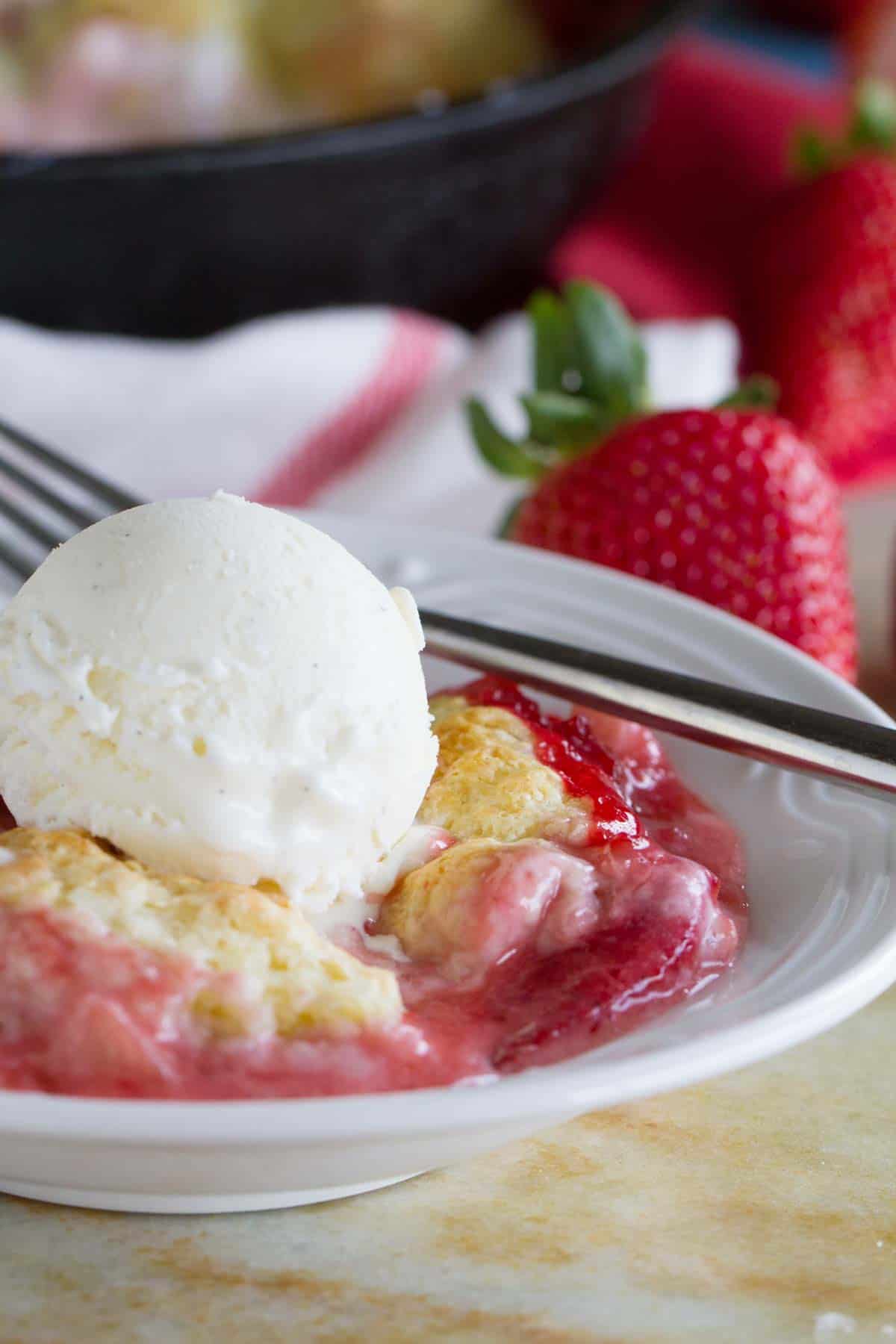 Bowl with strawberry cobbler with cream cheese with a scoop of ice cream on top.