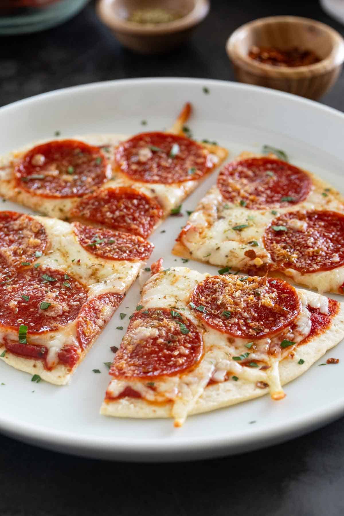 Tortilla pizza, topped with cheese and pepperoni, on a white plate.